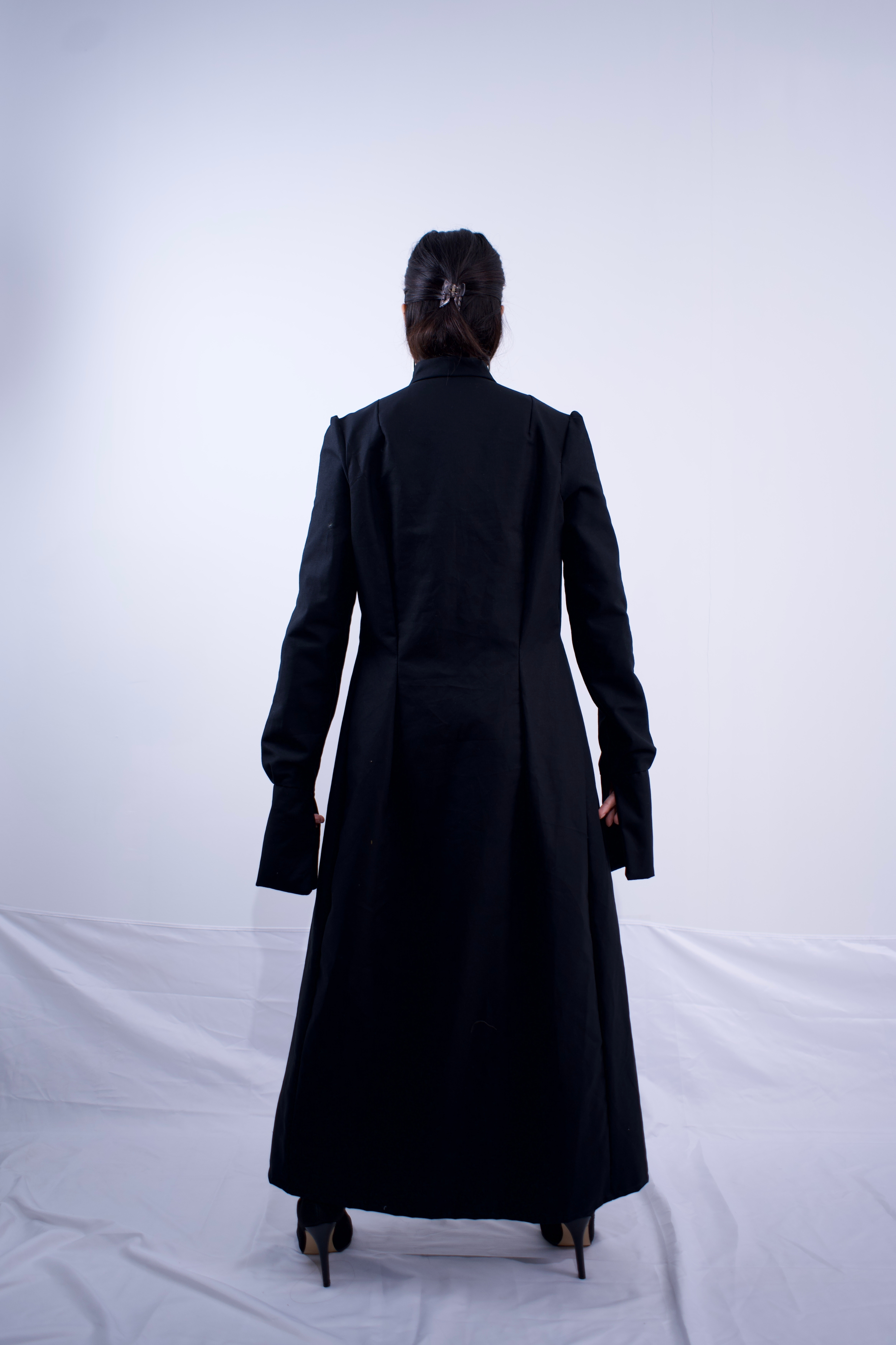 Person wearing a long black coat on a white background