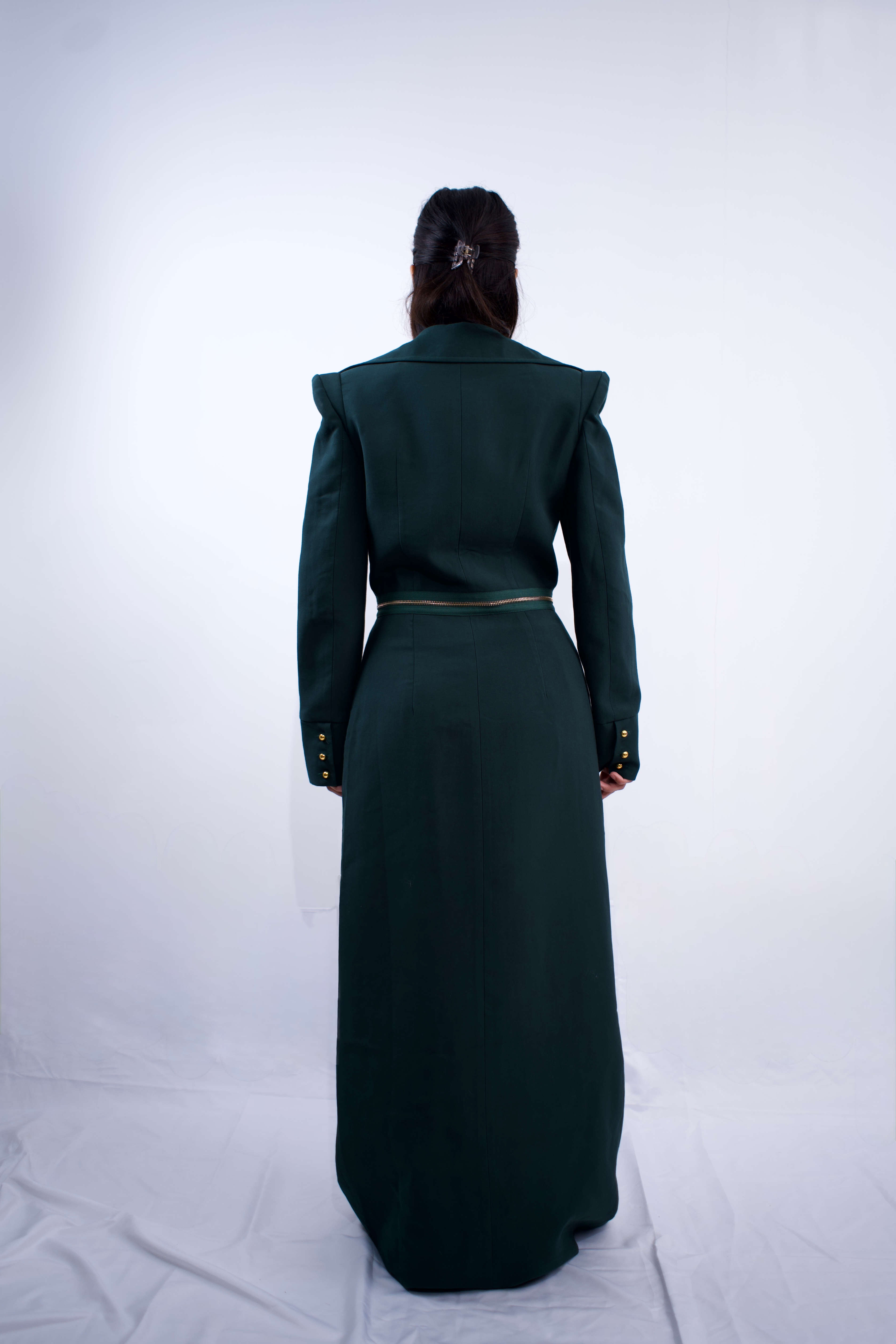 Person wearing a dark green outfit with a long dress and jacket on a white background