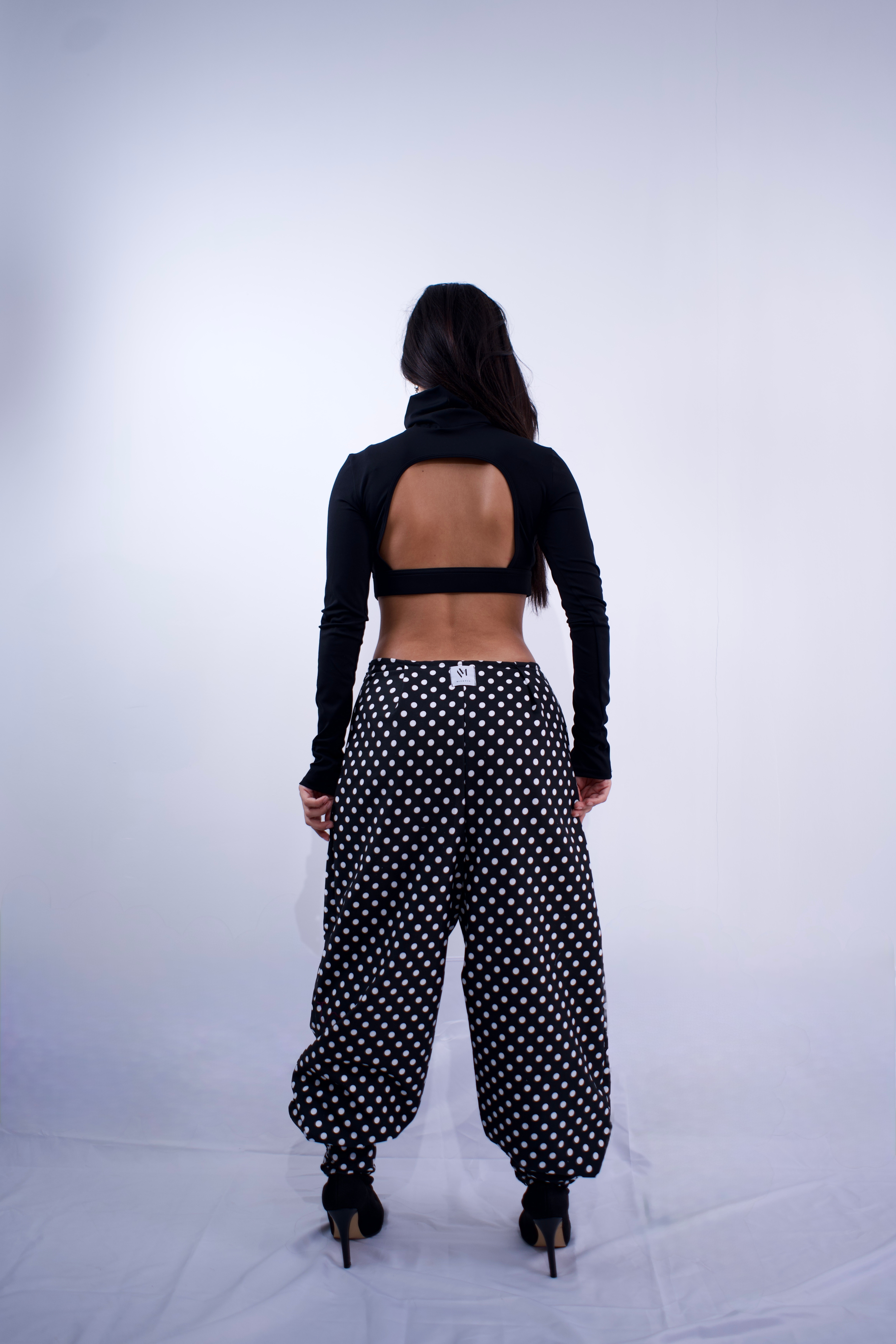 Person wearing a black long-sleeve crop top and polka dot pants on a white background