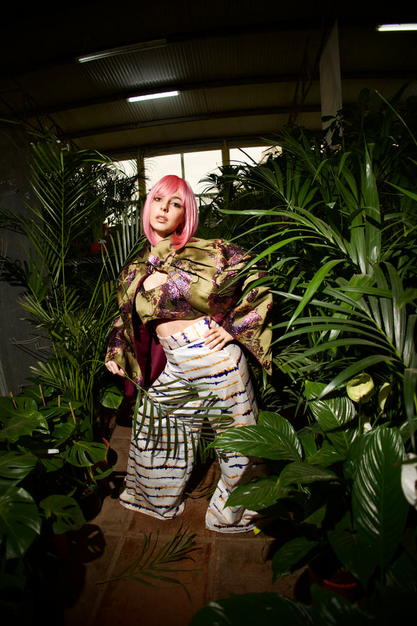 Person with pink hair standing among plants in a dimly lit indoor setting