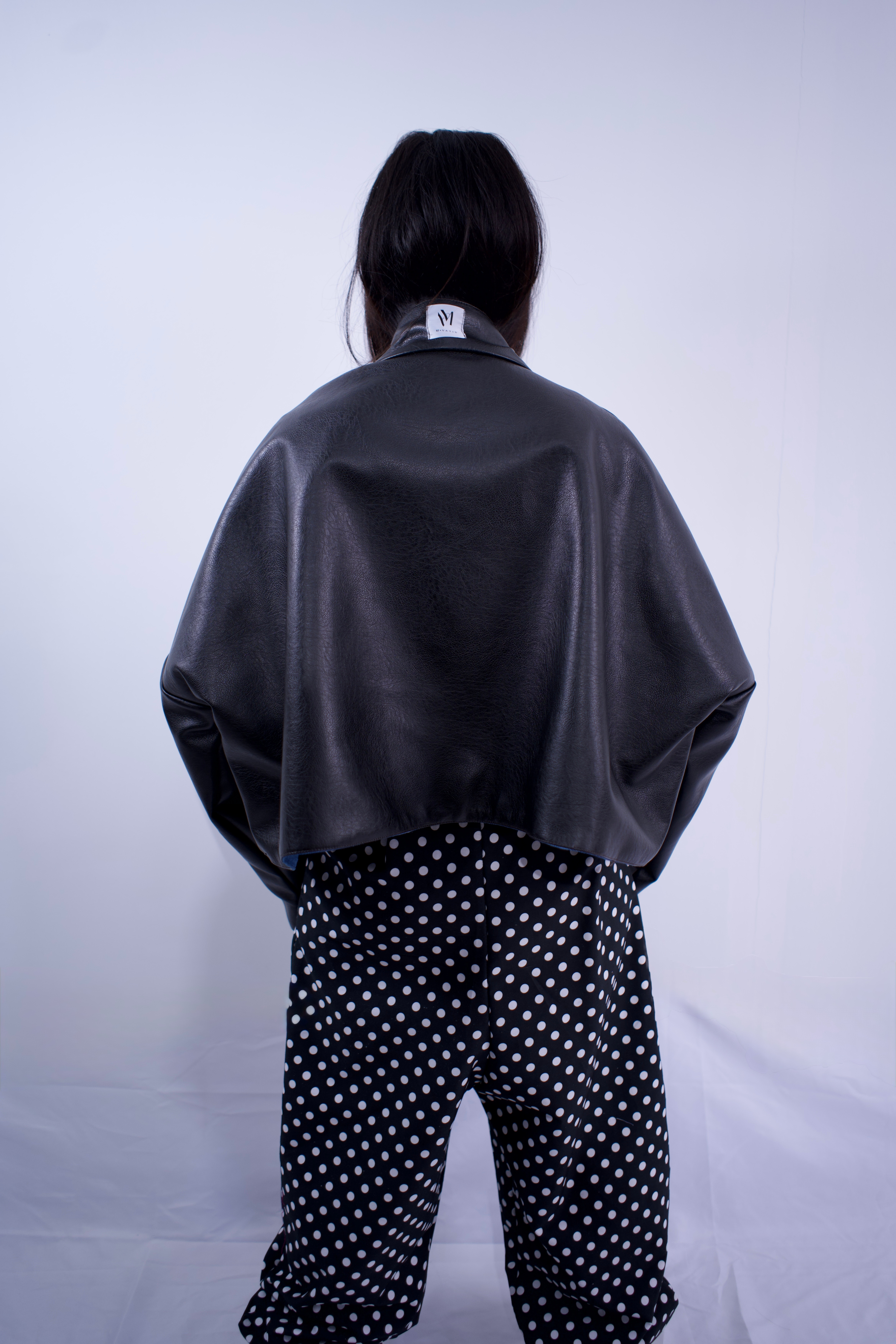 Person wearing a black leather jacket and polka dot pants on a plain background