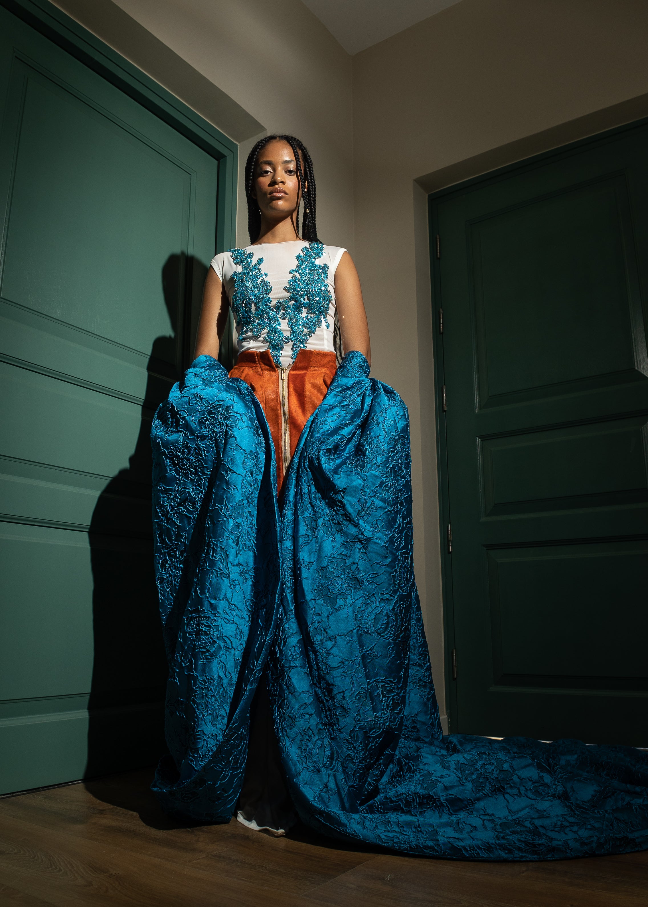 Designer evening gown with teal floral embroidery on a sheer mesh bodice, burnt orange velvet waistband, and a voluminous sapphire blue brocade skirt—perfect for formal events, galas, and red carpet occasions.”
