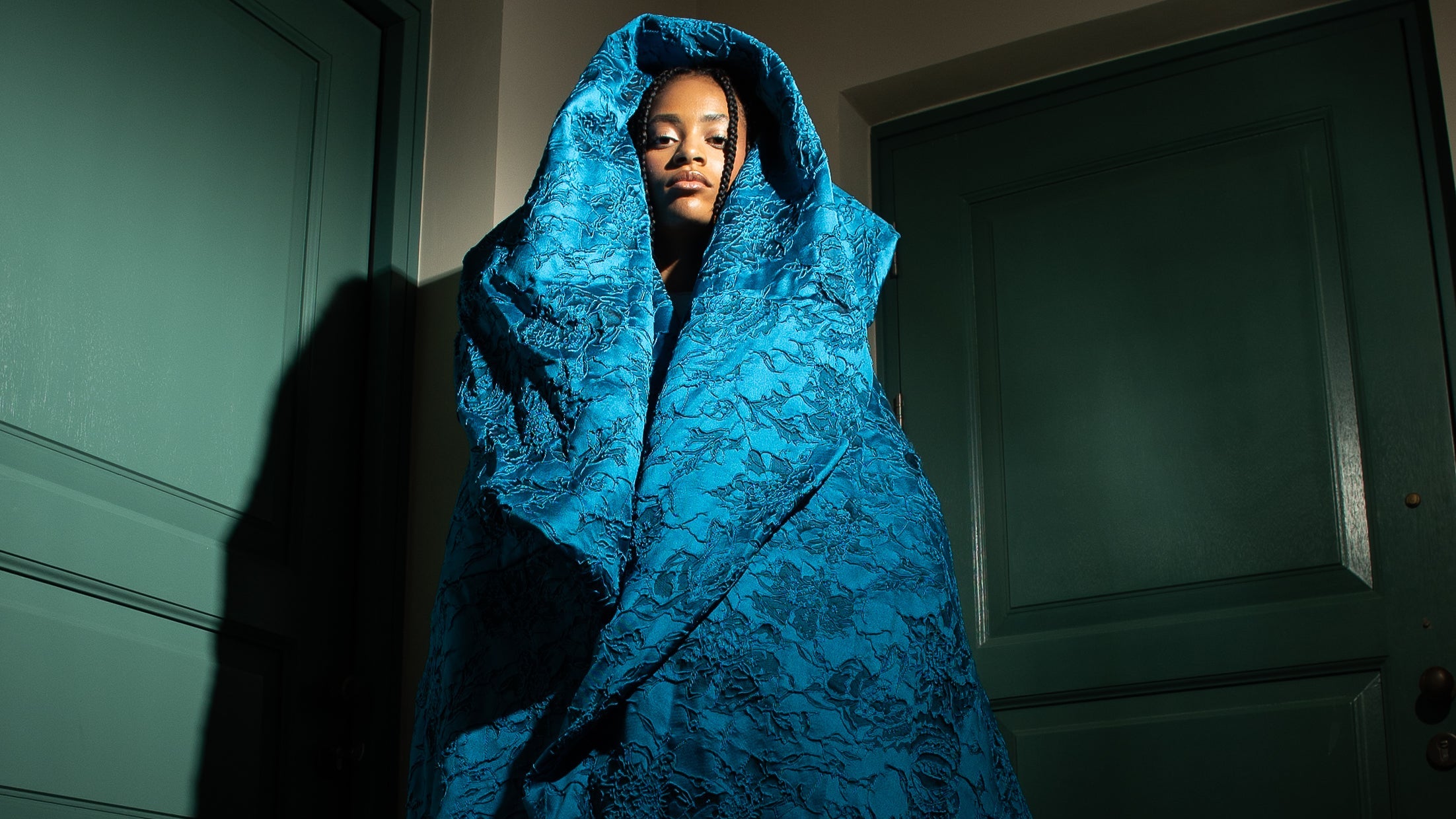 Designer evening gown with teal floral embroidery on a sheer mesh bodice, burnt orange velvet waistband, and a voluminous sapphire blue brocade skirt—perfect for formal events, galas, and red carpet occasions.”
