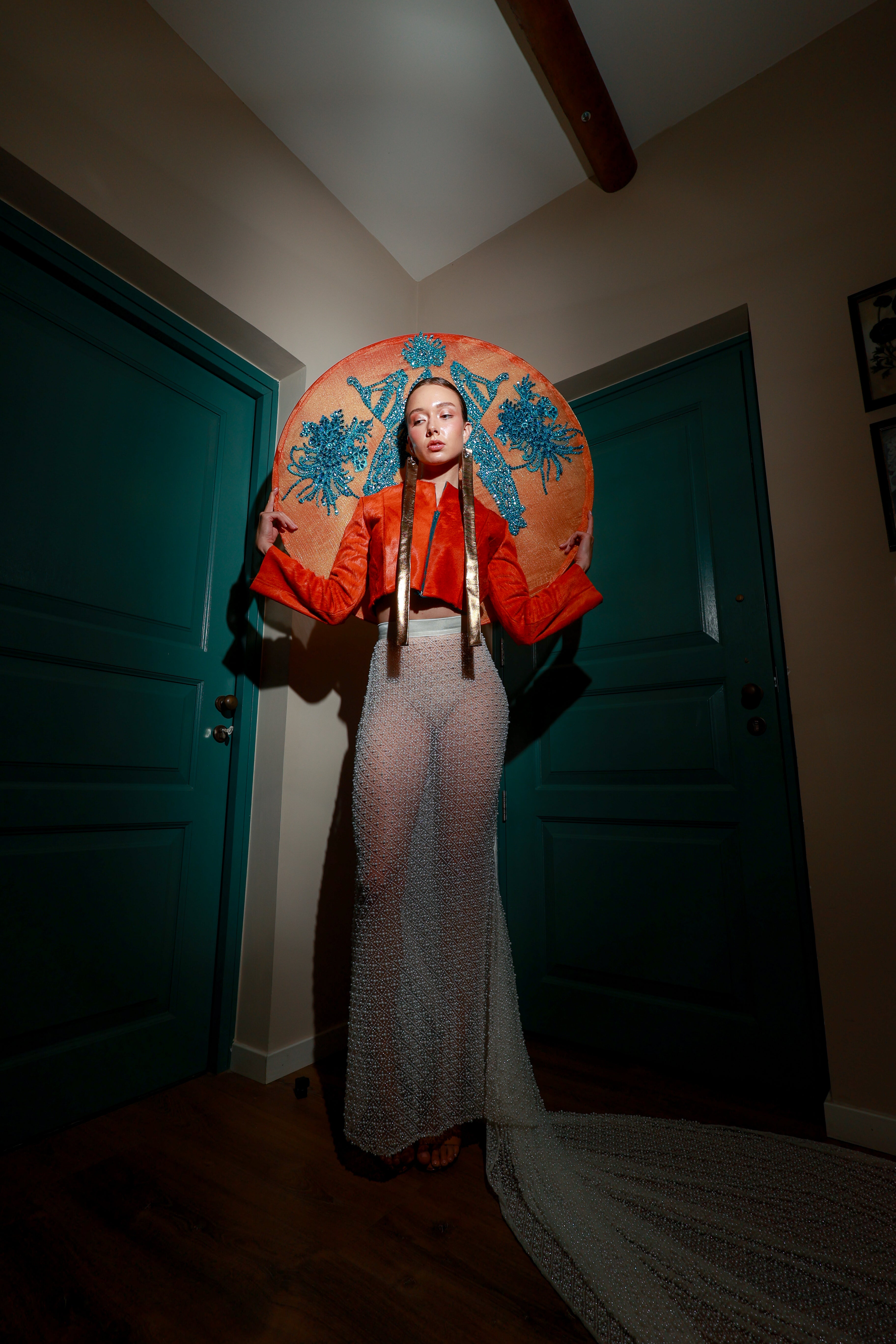 Model wearing a burnt orange genuine leather cowhide cropped jacket paired with a hand-beaded sheer crystal mesh maxi skirt with a long sweeping train — modern avant-garde fashion look.
High-fashion outfit featuring an orange leather crop jacket with suede strap accents and a transparent crystal mesh skirt with intricate beading — luxury designer set.
