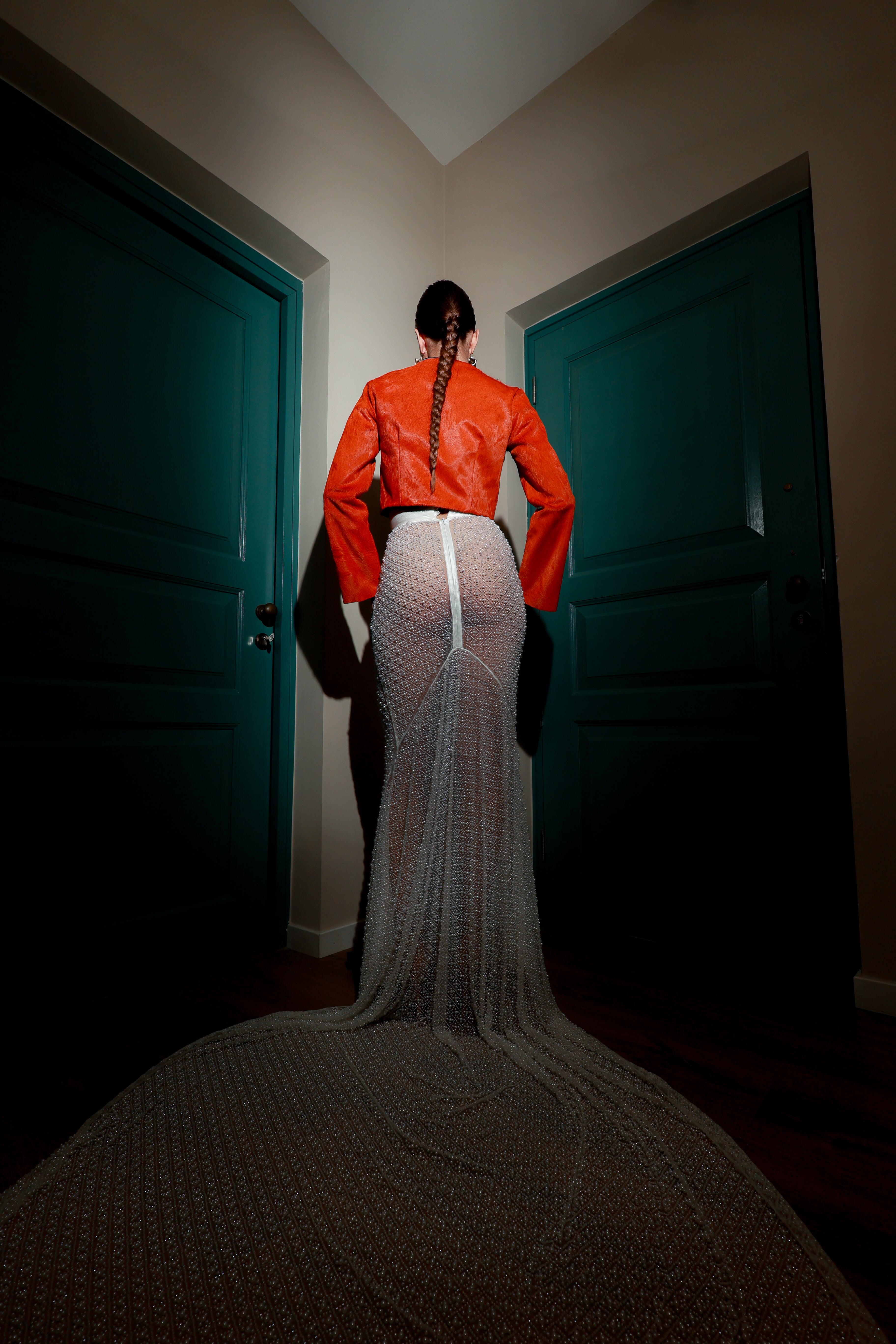 Model wearing a burnt orange genuine leather cowhide cropped jacket paired with a hand-beaded sheer crystal mesh maxi skirt with a long sweeping train — modern avant-garde fashion look.
High-fashion outfit featuring an orange leather crop jacket with suede strap accents and a transparent crystal mesh skirt with intricate beading — luxury designer set.
