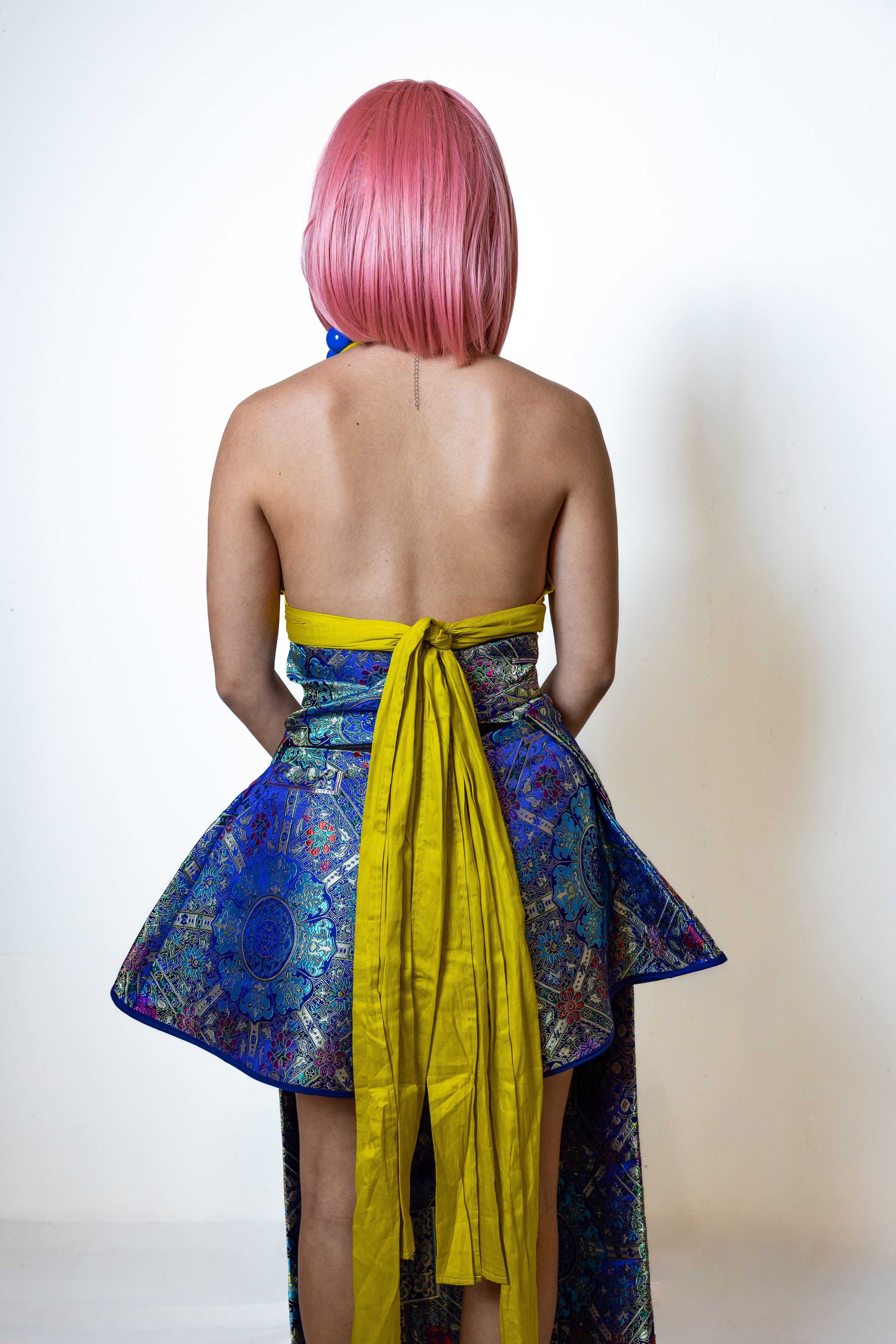 Person wearing a colorful dress with a yellow belt on a plain background
