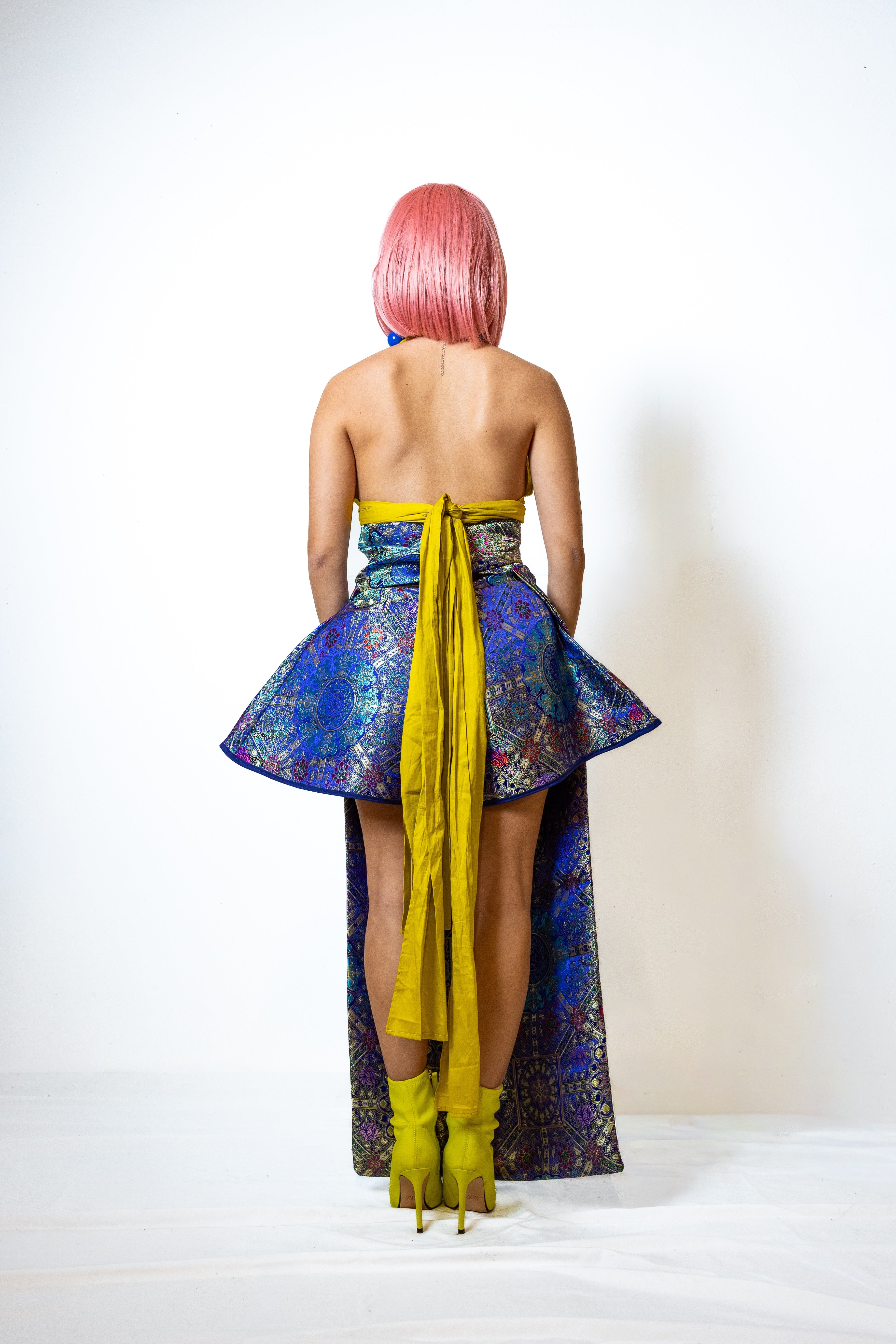 Person wearing a colorful strapless dress with a yellow sash on a white background