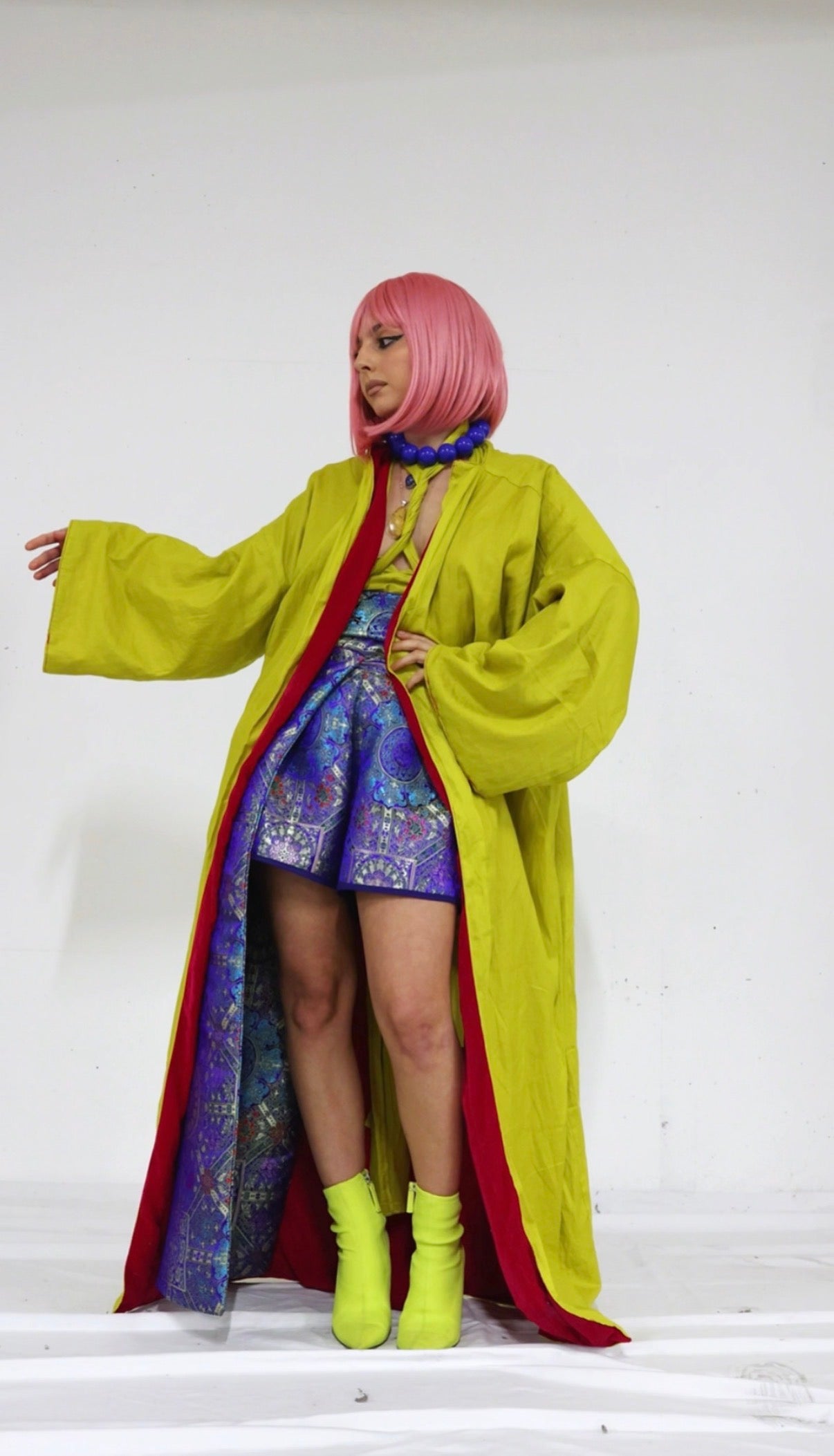 Person wearing a bright yellow coat with a colorful patterned dress underneath on a white background