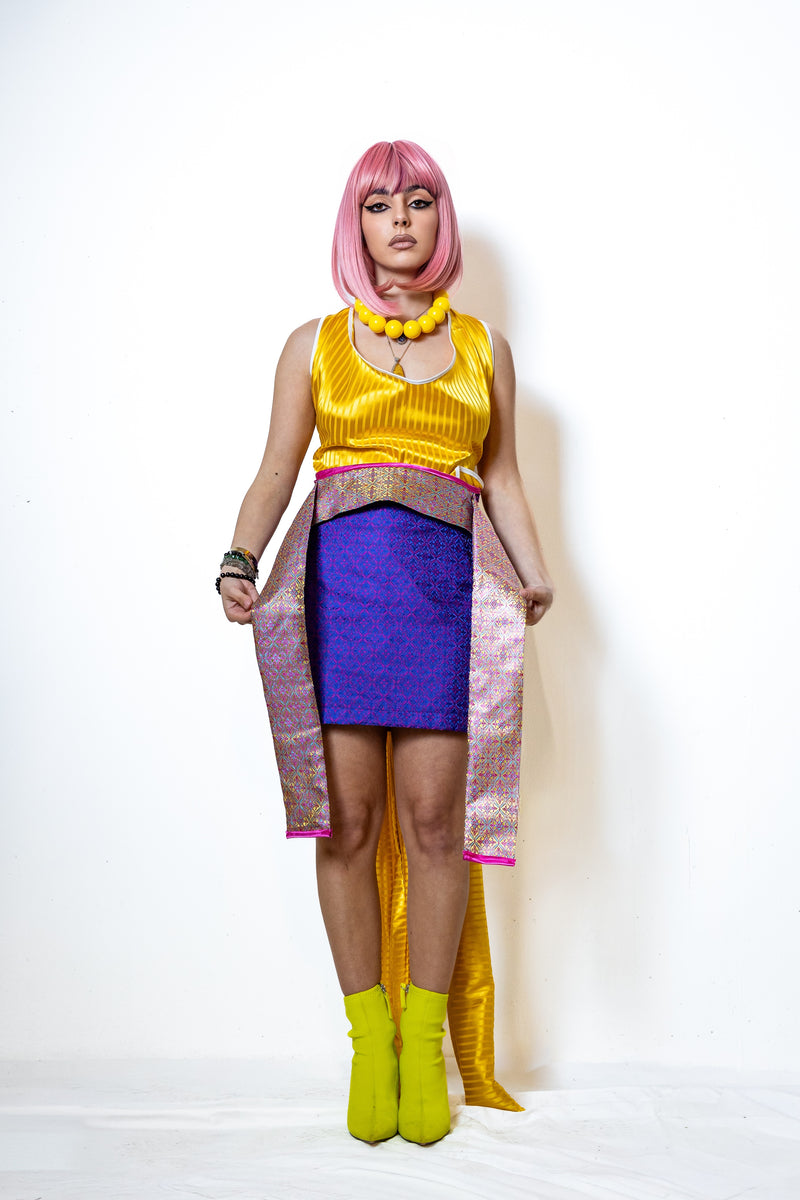 Person wearing a yellow top, purple skirt, and green boots with a pink wig on a white background