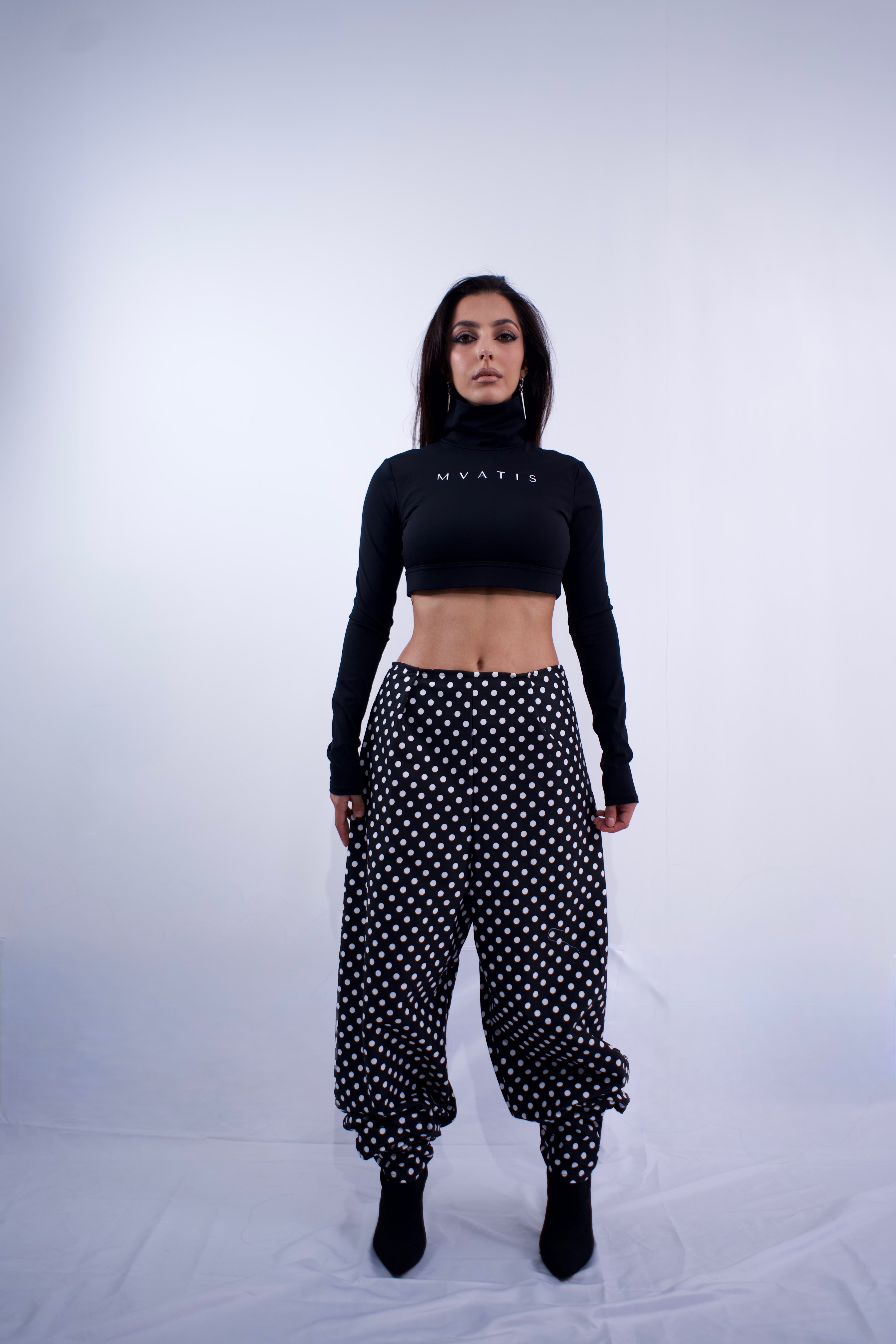 Woman wearing a black crop top and polka dot pants on a white background