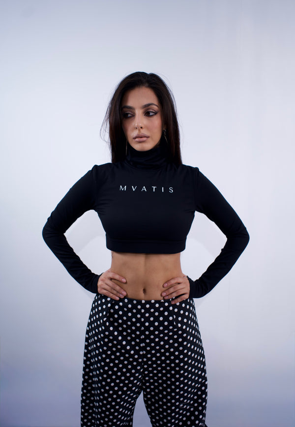 Woman wearing a black crop top with 'MVATIS' branding and polka dot pants on a light gray background