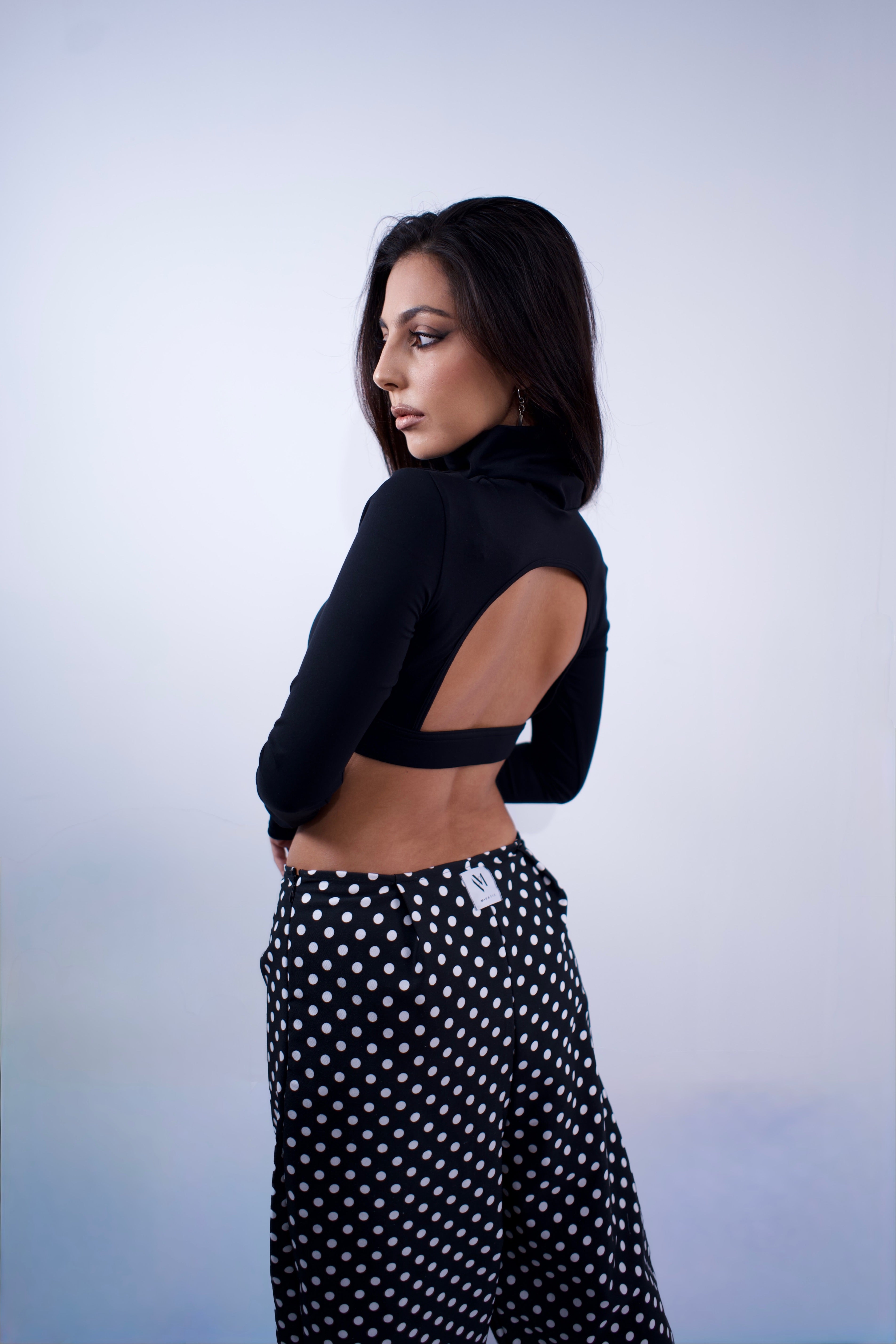 Woman wearing a black cut-out top and polka dot pants against a light blue background