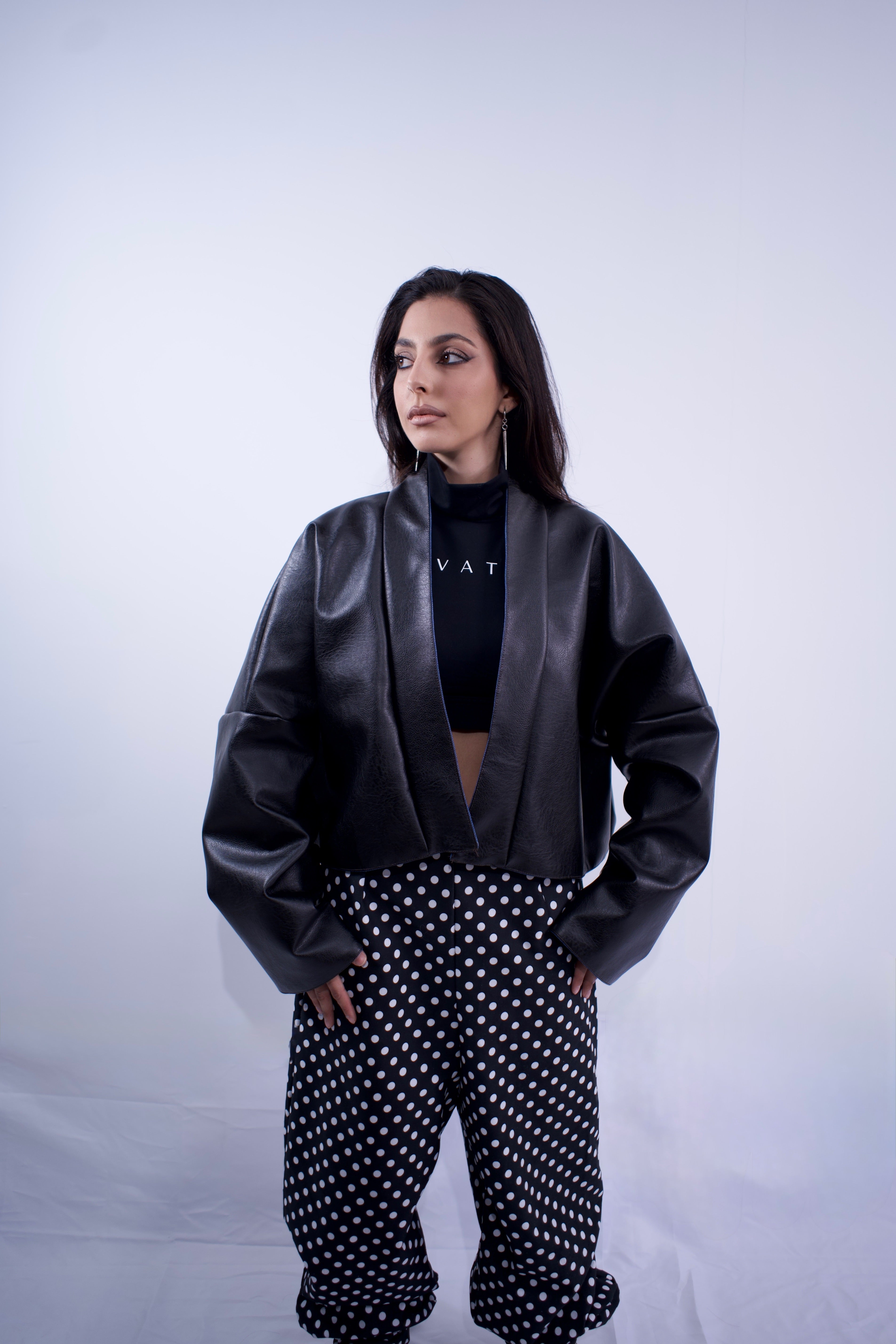 Person wearing a black leather jacket and polka dot pants on a white background