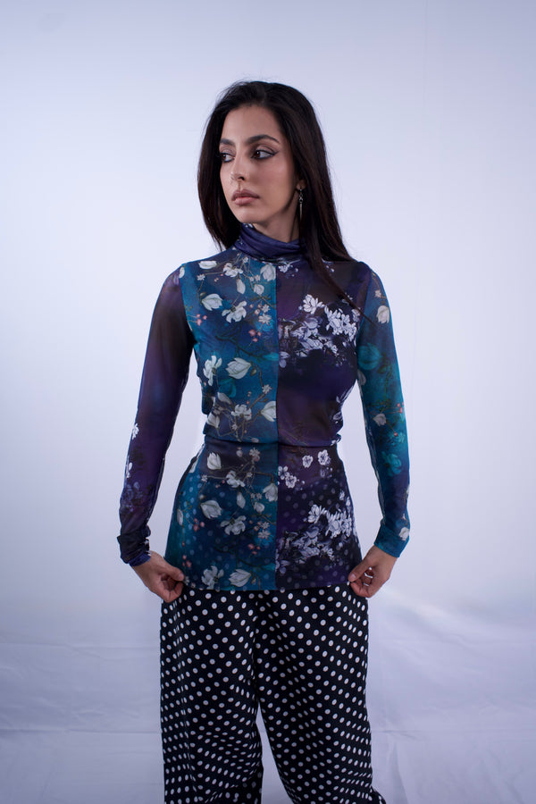 Woman wearing a floral patterned top and black pants with white patterns on a white background