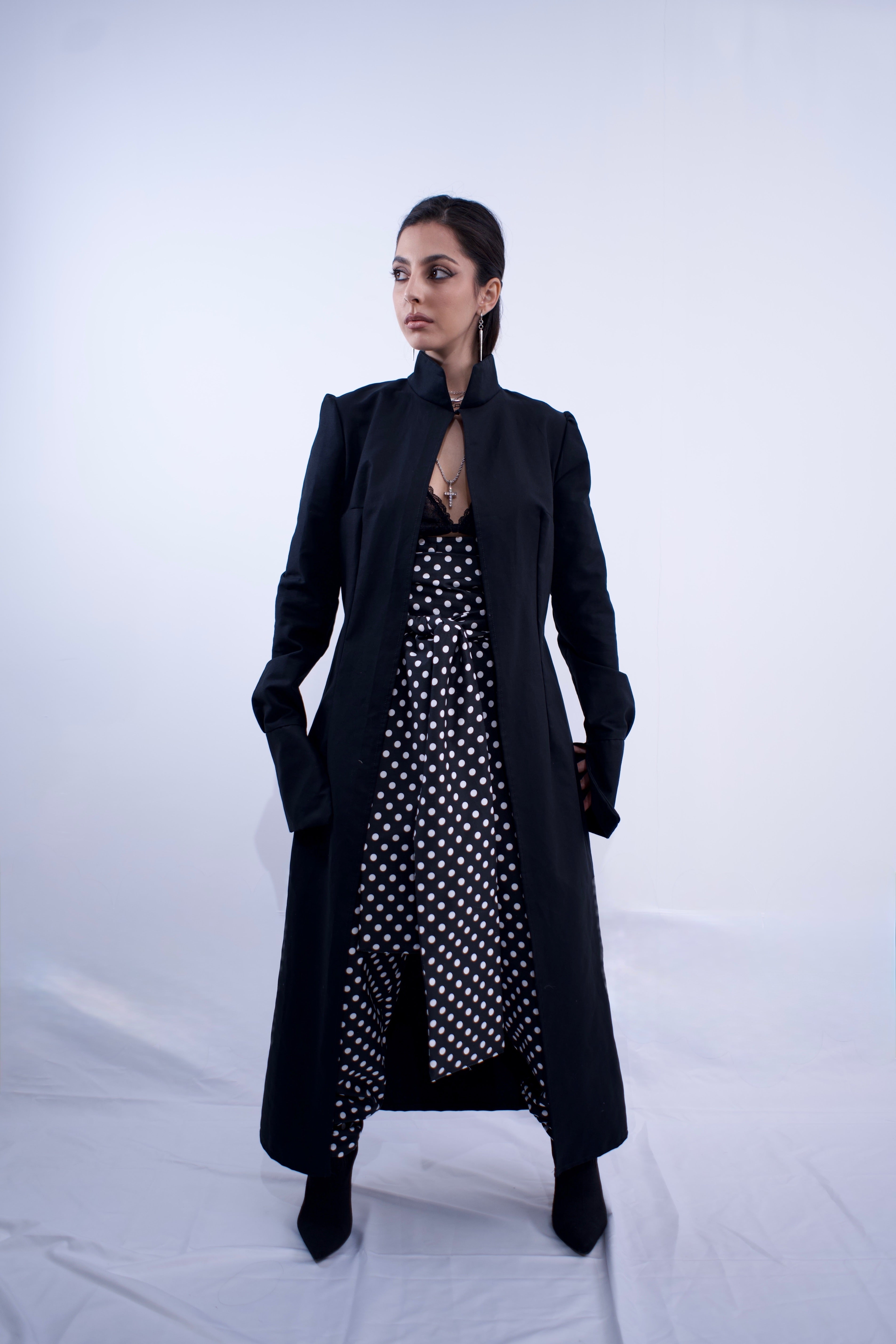Woman wearing a long black coat over a polka dot dress on a white background
