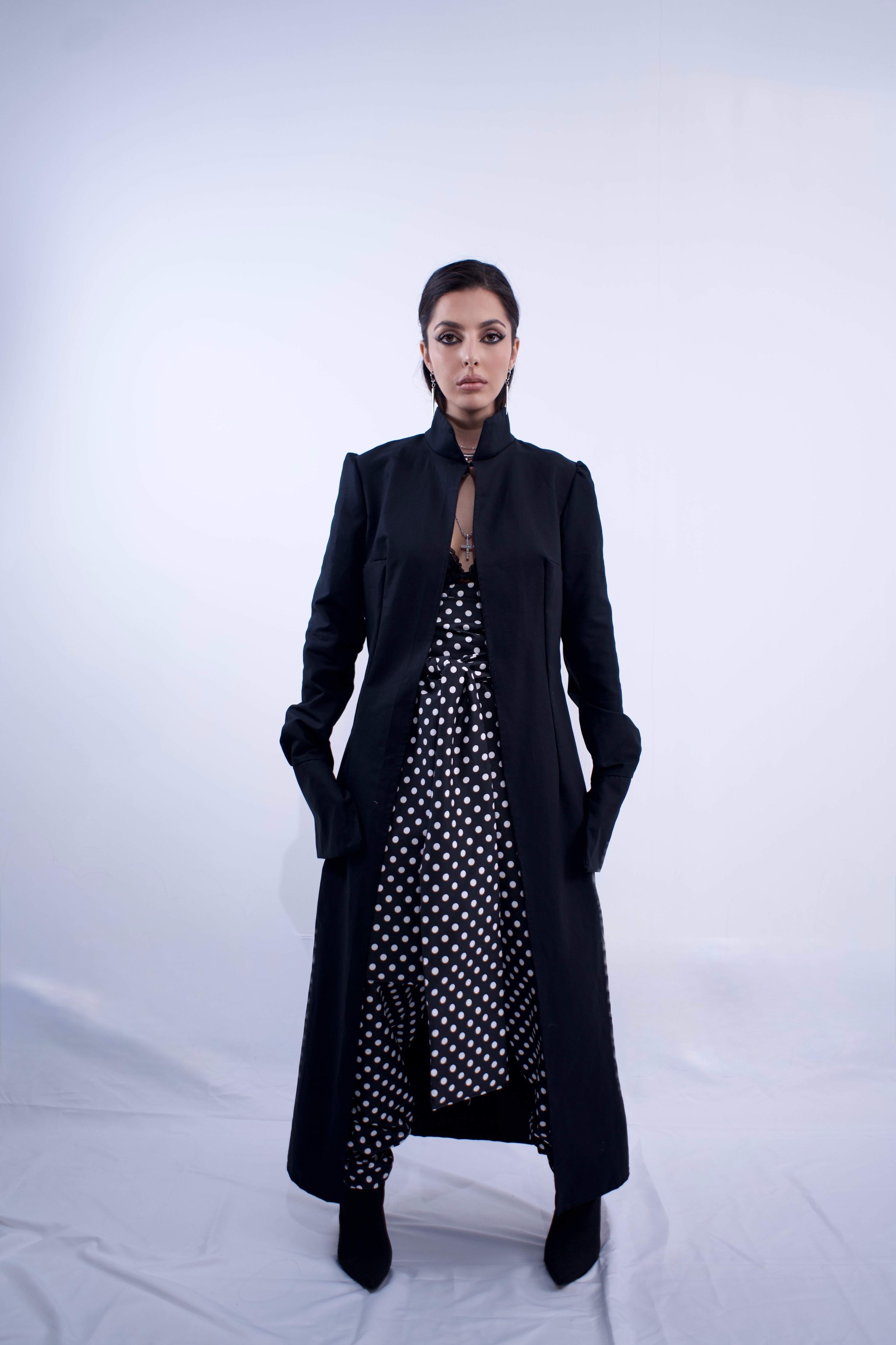 Woman wearing a long black coat over a polka dot dress on a white background