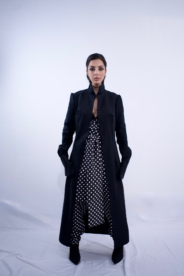 Woman wearing a long black coat over a polka dot dress on a white background