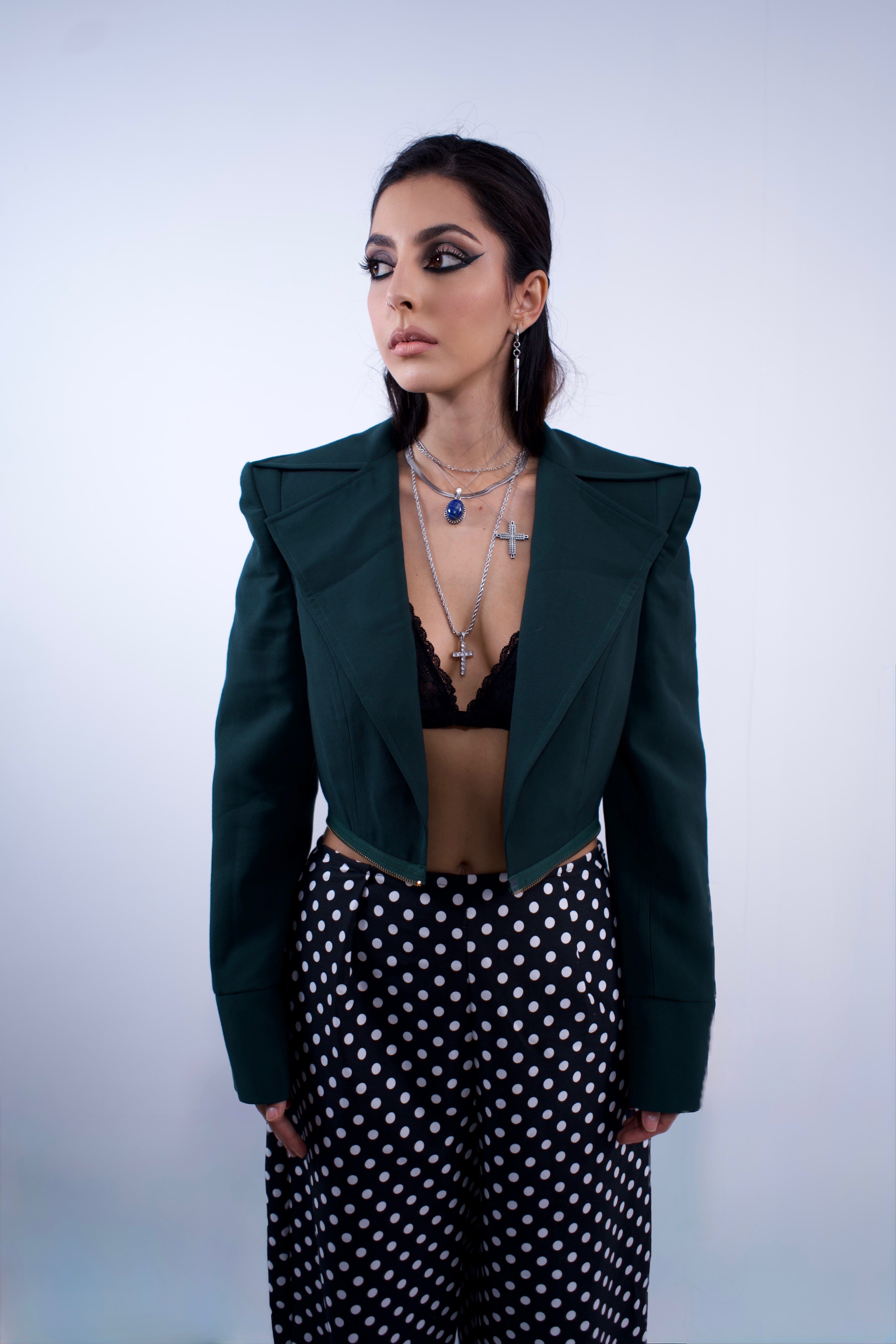 Woman wearing a dark green jacket, black top, and polka dot pants against a light background