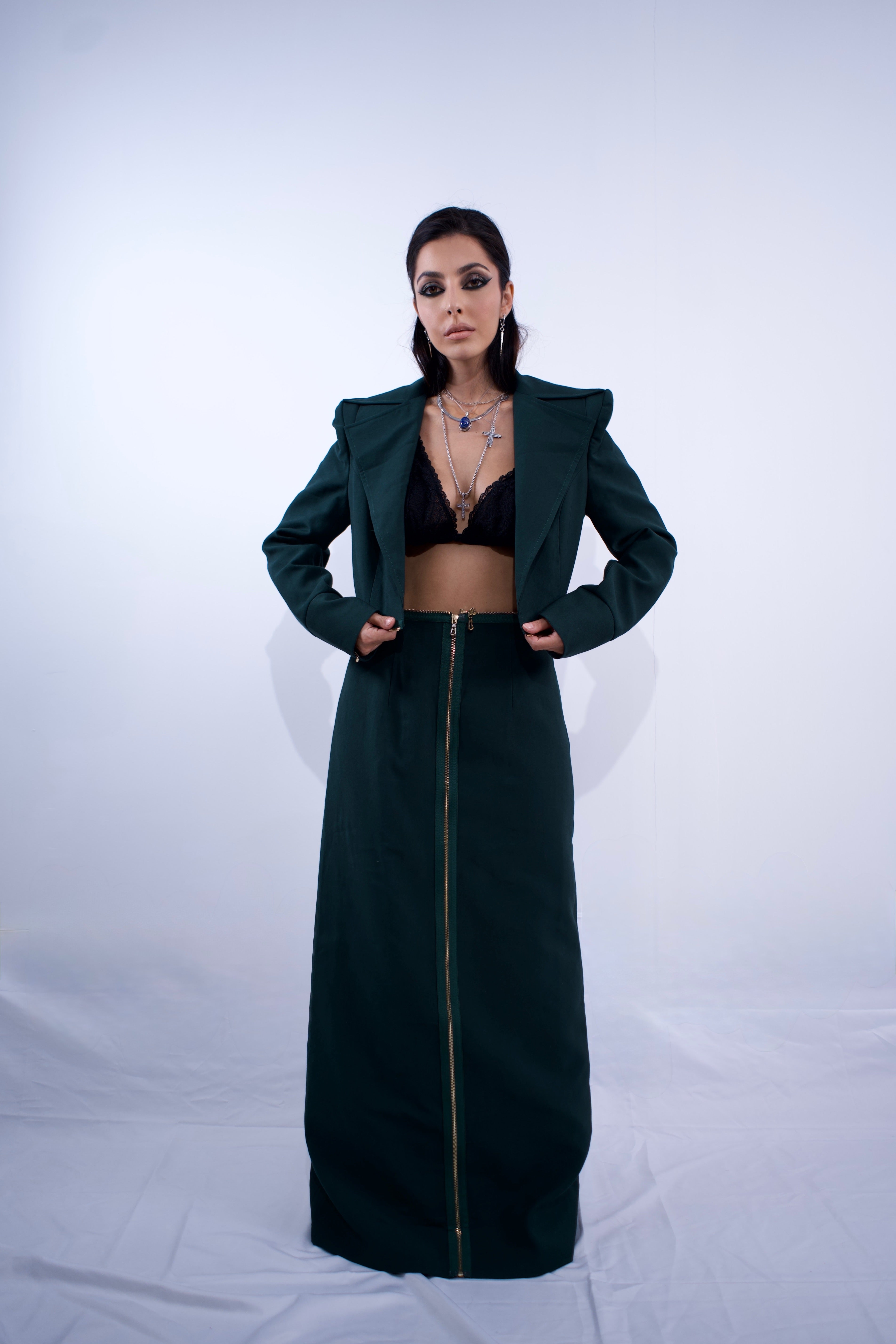 Person wearing a long dark green coat over a black outfit on a white background