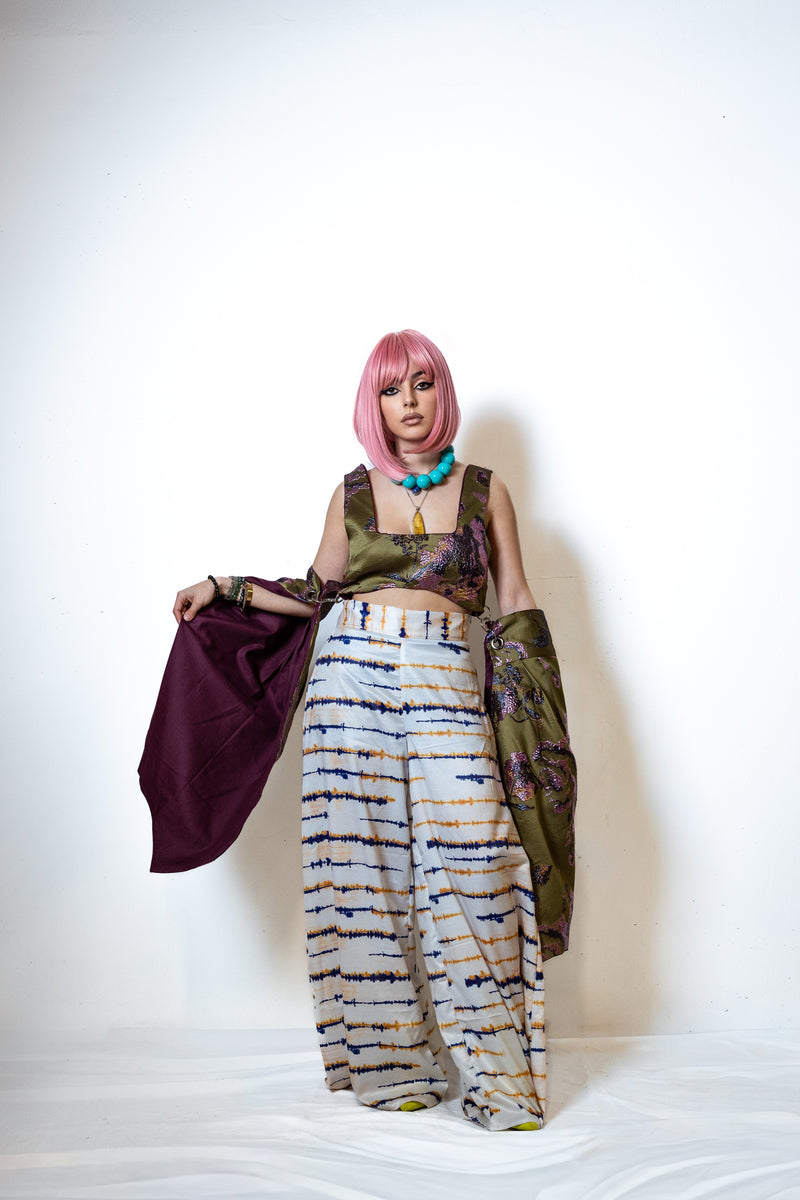 Model wearing a colorful outfit with tie-dye pants and a patterned top against a white background