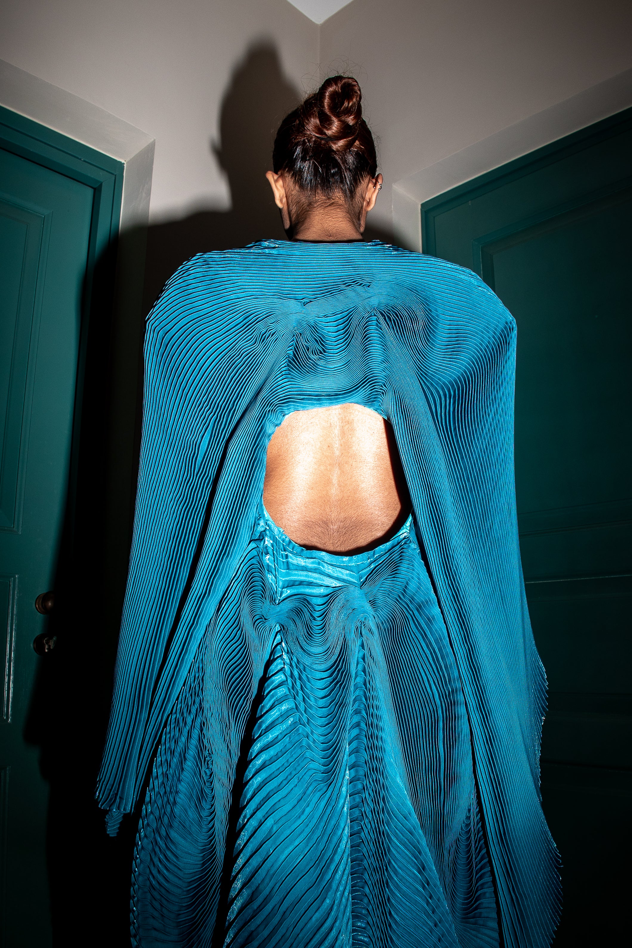 Teal accordion pleated dress with hand-stitched detailing and a distinctive circular design at the center.
