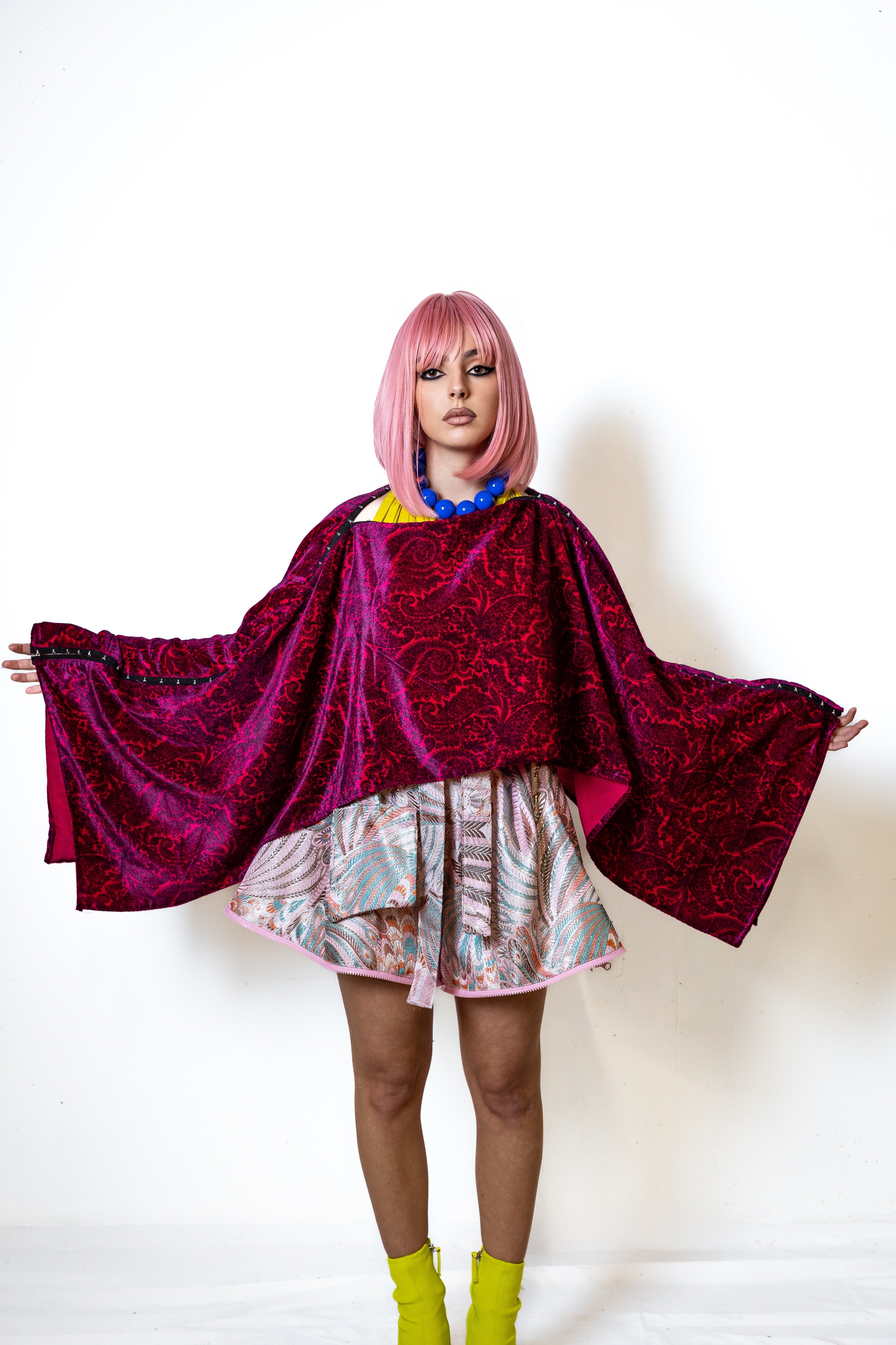 Person wearing a vibrant magenta paisley velvet outfit with a white background
