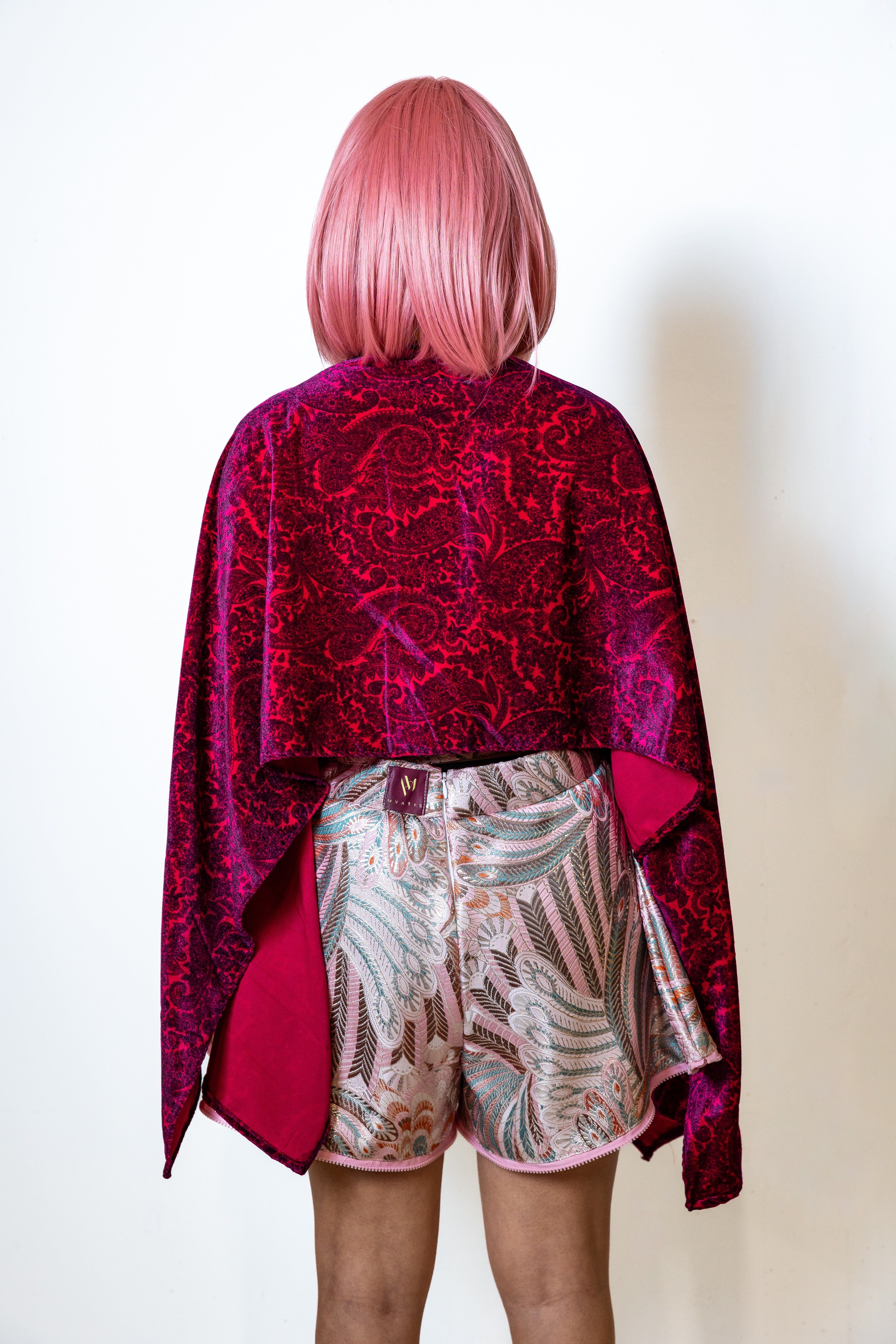 Person wearing a patterned red magenta paisley printed top with floral shorts on a plain background